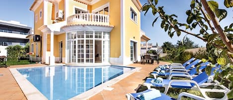 A yellow building with a pool and lounge chairs.