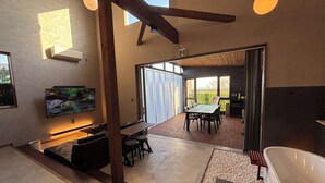 A modern interior with a dining area, a large flat-screen TV, a bathtub, and a view through a glass door. - Villa CORTILE (Awaji)