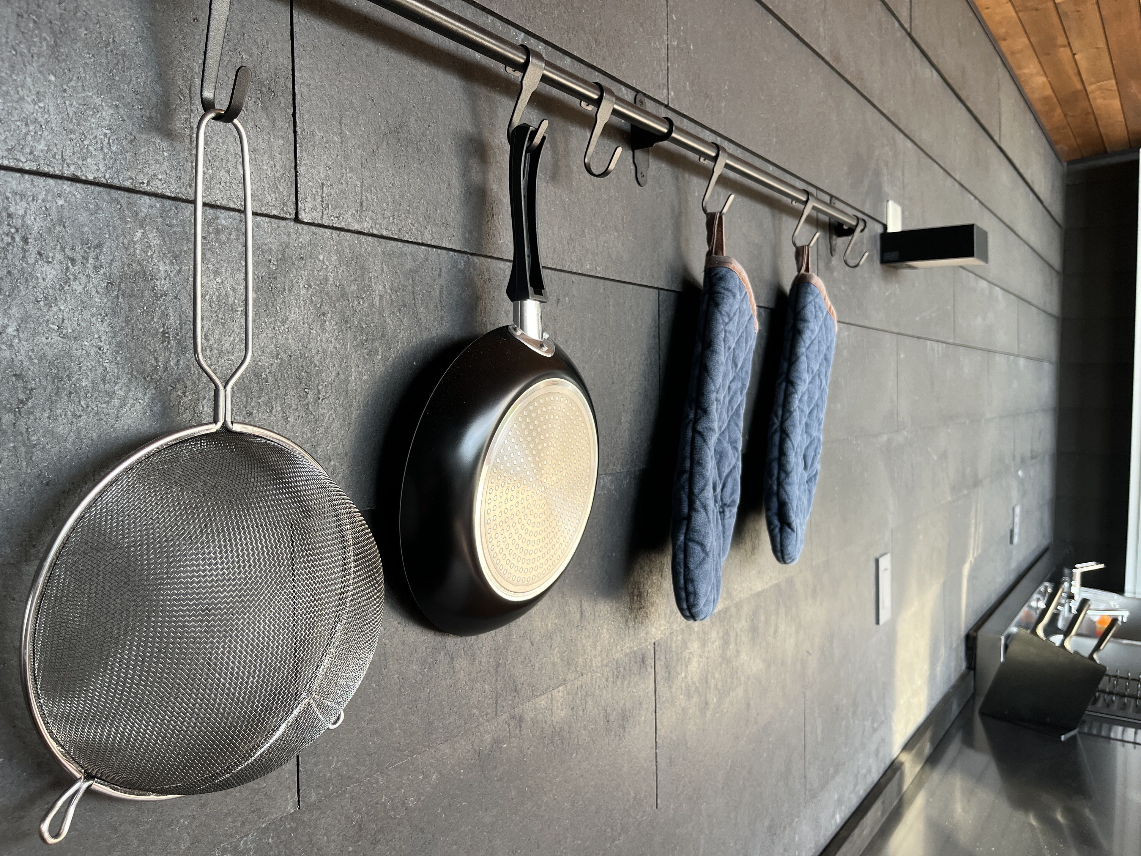 A kitchen with a hanging rack holding a strainer, a frying pan, and two pots.