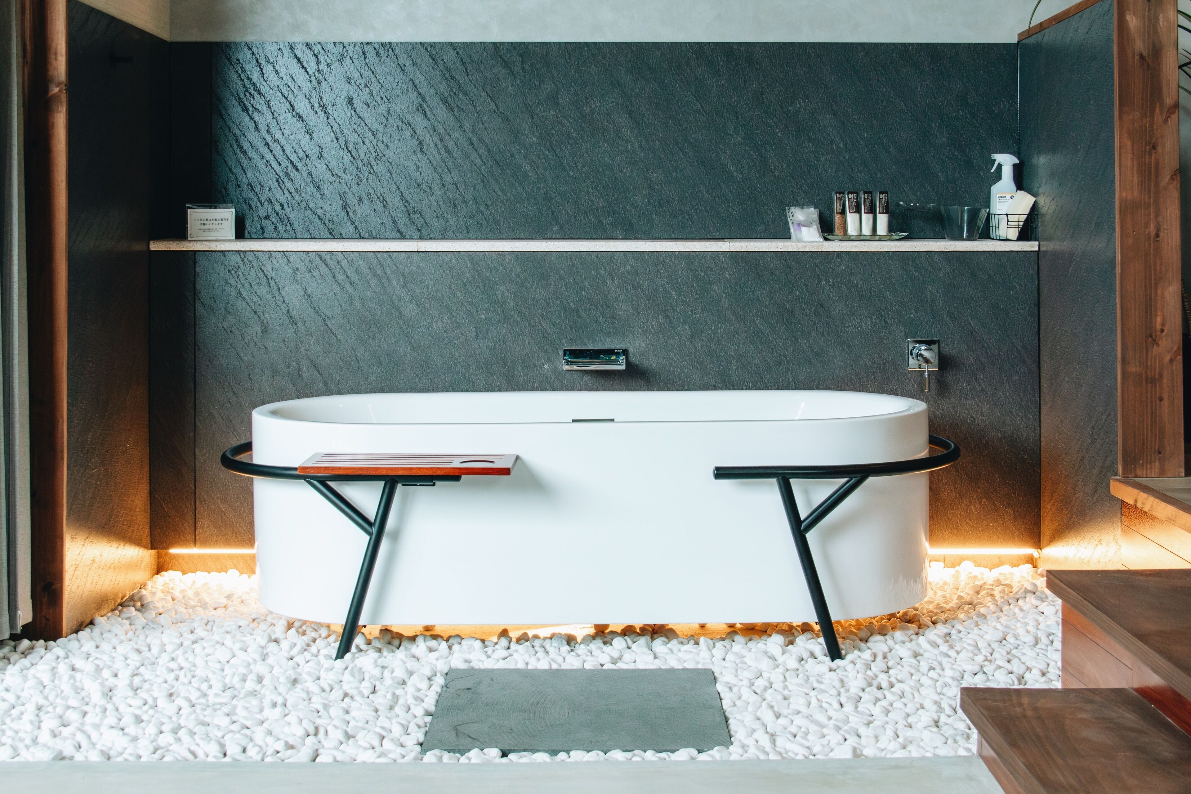 A modern bathroom with a freestanding bathtub, white pebbles, and a wooden floor.