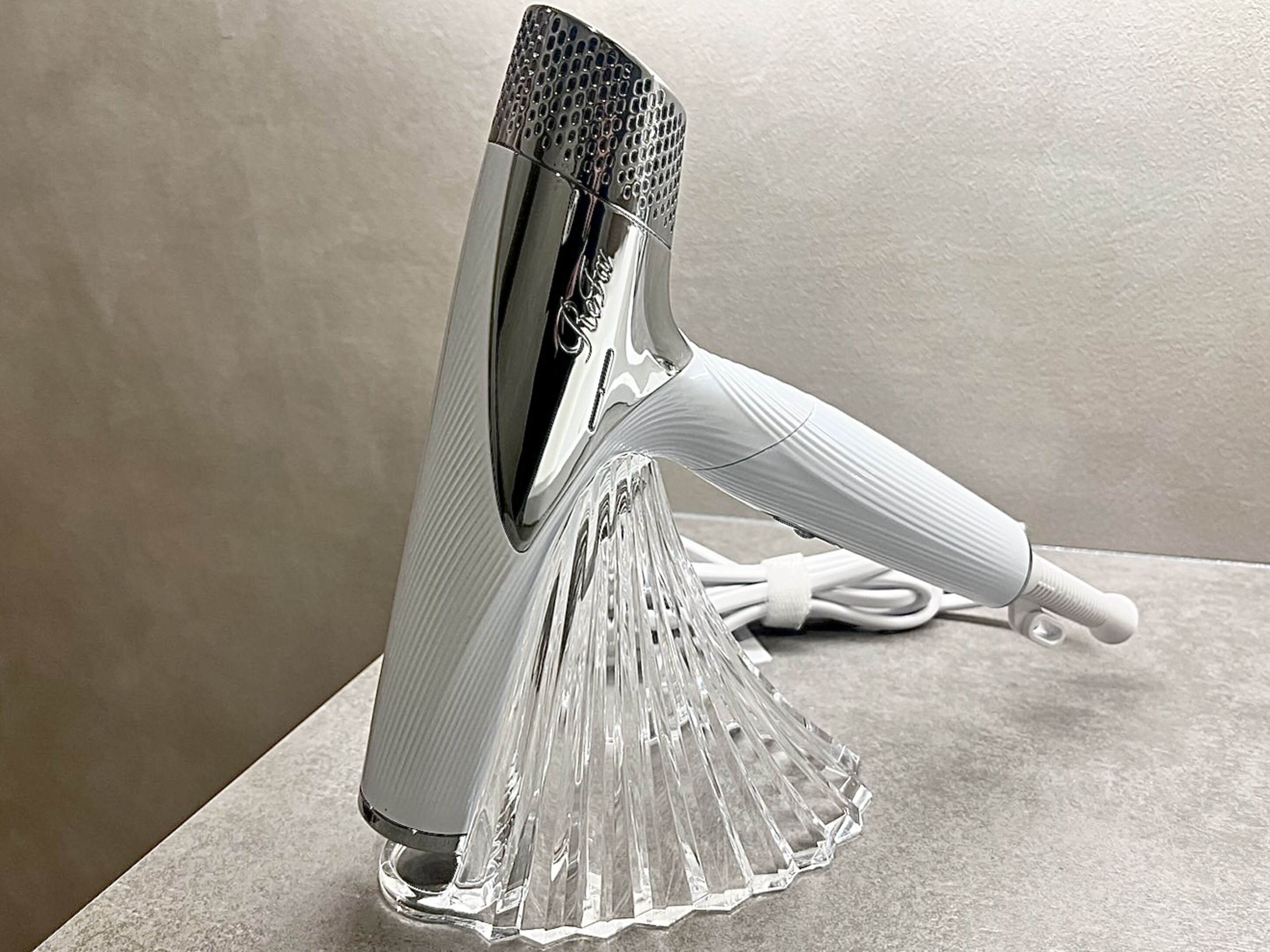 A clear, modern, metallic hairdryer with a ribbed handle and a transparent base, placed on a flat surface.