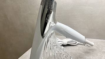 A clear, modern, metallic hairdryer with a ribbed handle and a transparent base, placed on a flat surface.