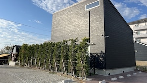 A modern building with a flat roof, a large window, and a paved area with trees. - Villa CORTILE (Awaji)