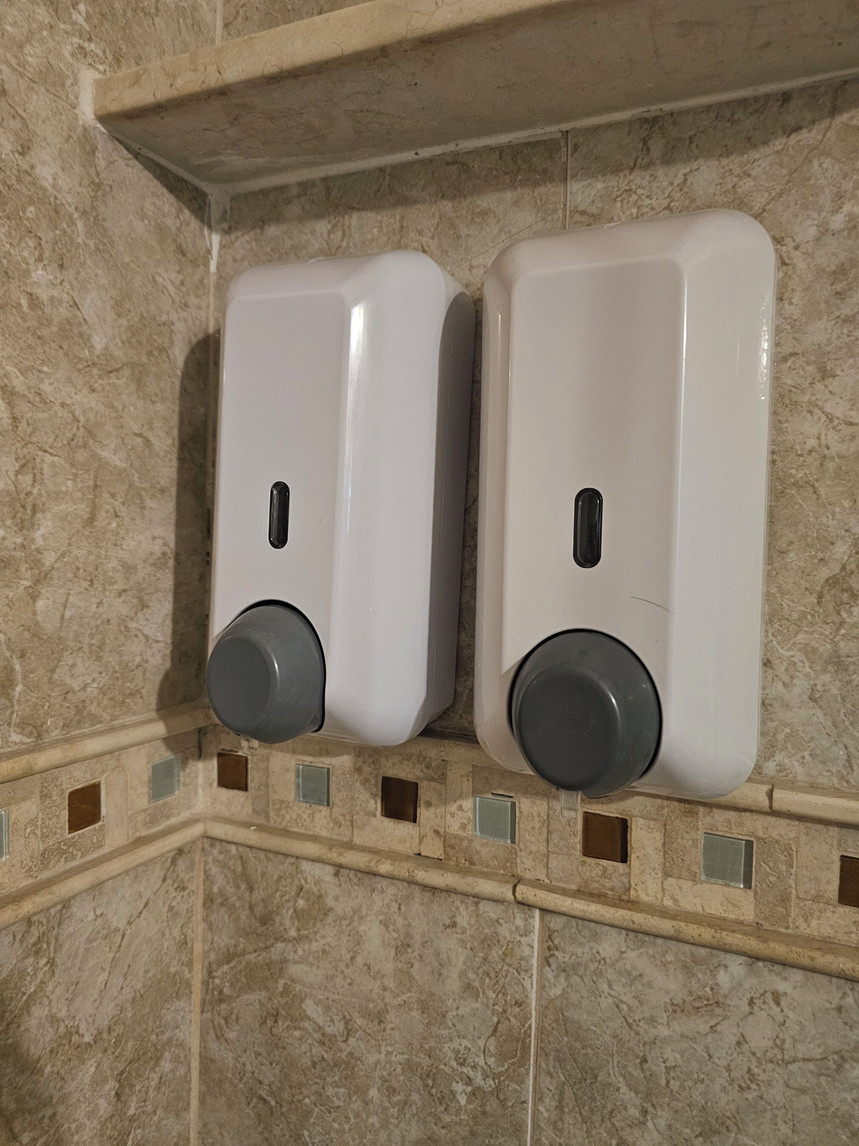 Two wall-mounted soap dispensers in a bathroom with tiled walls and a decorative border.