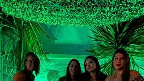 Un grupo de personas sentadas en sillones blancos en una habitación con iluminación ambiental verde y un techo decorativo.