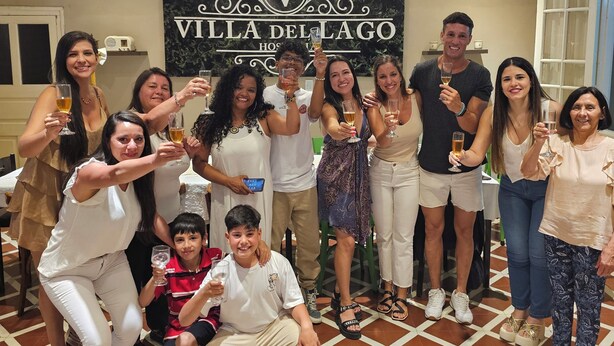 Un grupo de personas en un evento social en una habitación con piso de baldosas y un cartel que dice "VILLA DEL LAGO".