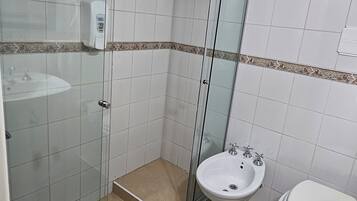 Une salle de bain avec une douche à parois de verre, un lavabo sur colonne et des toilettes.