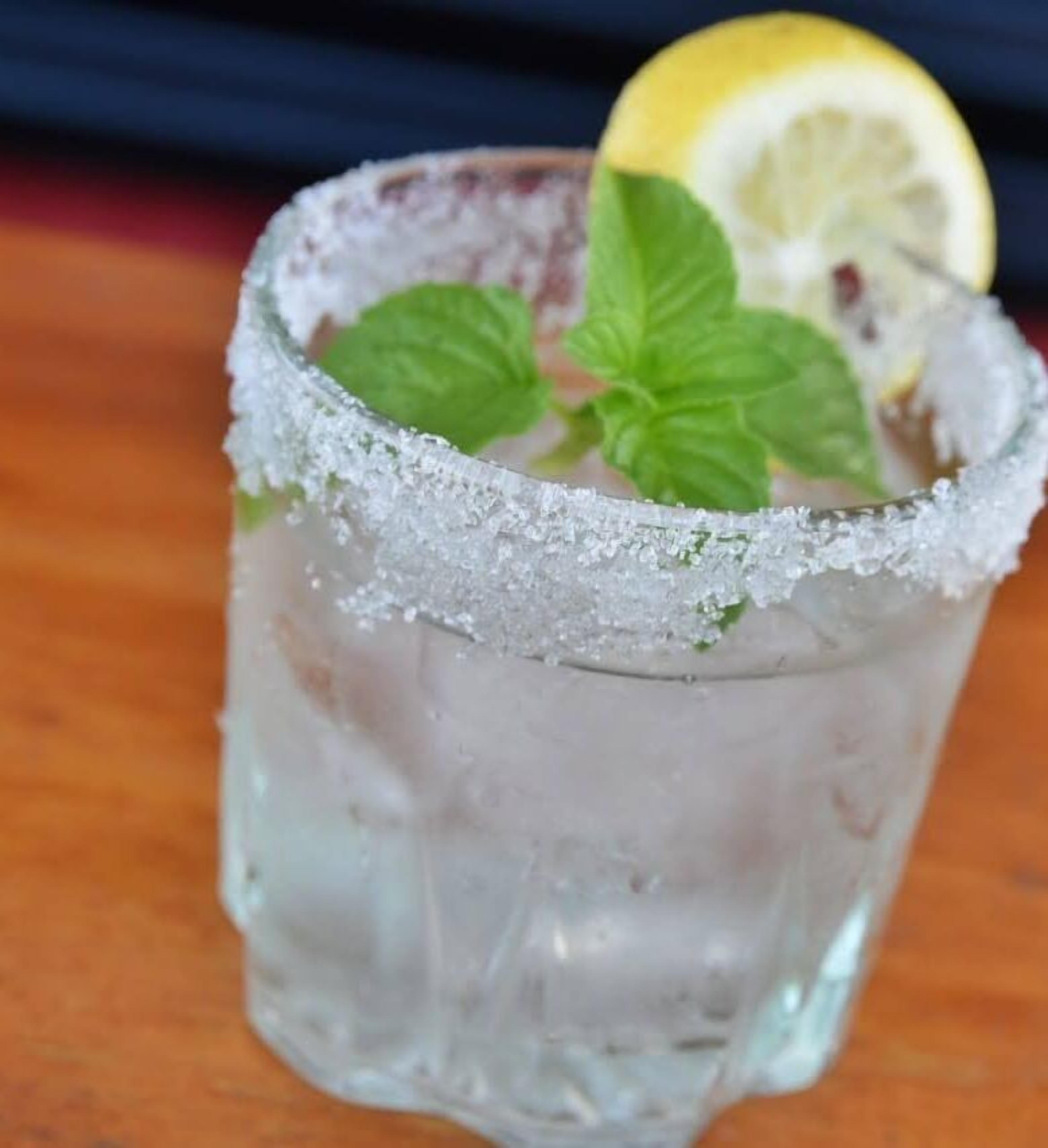 Un verre dont le bord est saupoudré de sel, garni de feuilles de menthe et d’une tranche de citron.