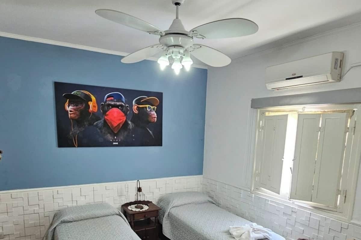 Habitación de hotel con dos camas individuales, ventilador de techo, un cuadro en la pared y ventana con cortinas.