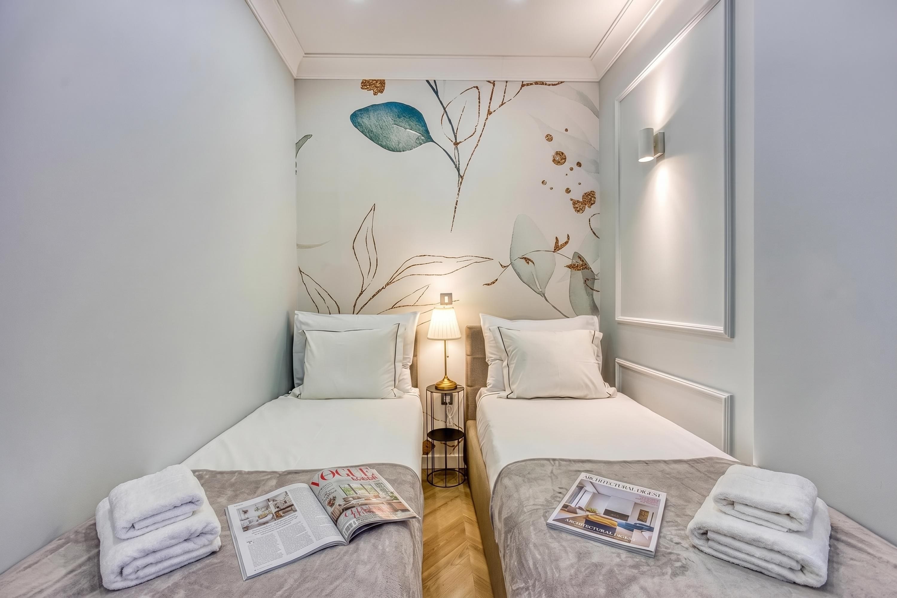 Habitación de hotel con dos camas, una mesita de noche, una lámpara y una revista sobre la cama.