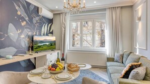 A modern living room with a round dining table set for four, a sofa, a TV, and a large window with curtains.