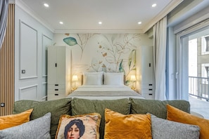 A bedroom with a bed, two bedside lamps, a green sofa, and a wall with a floral mural. - Boutique Downtown Studio with Balcony  1 (Zagreb)
