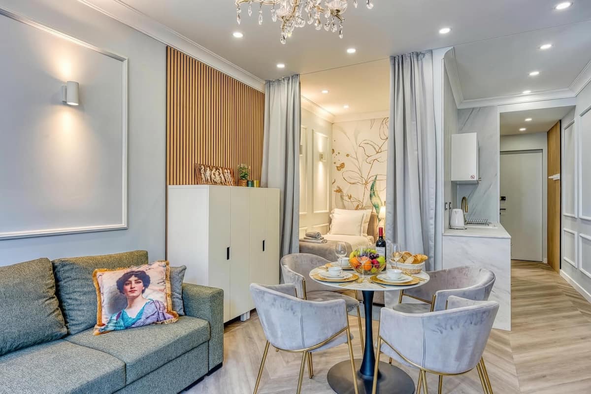 Un salon moderne avec un canapé, une table à manger et des chaises, un lustre et, au fond, un coin cuisine.