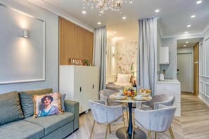 A modern living room with a sofa, a dining table with chairs, a chandelier, and a kitchen area in the background. - Boutique Downtown Studio with Balcony  1 (Zagreb)