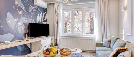 Een moderne woonkamer met een flatscreen televisie, een eettafel voor twee personen en een comfortabele bank.