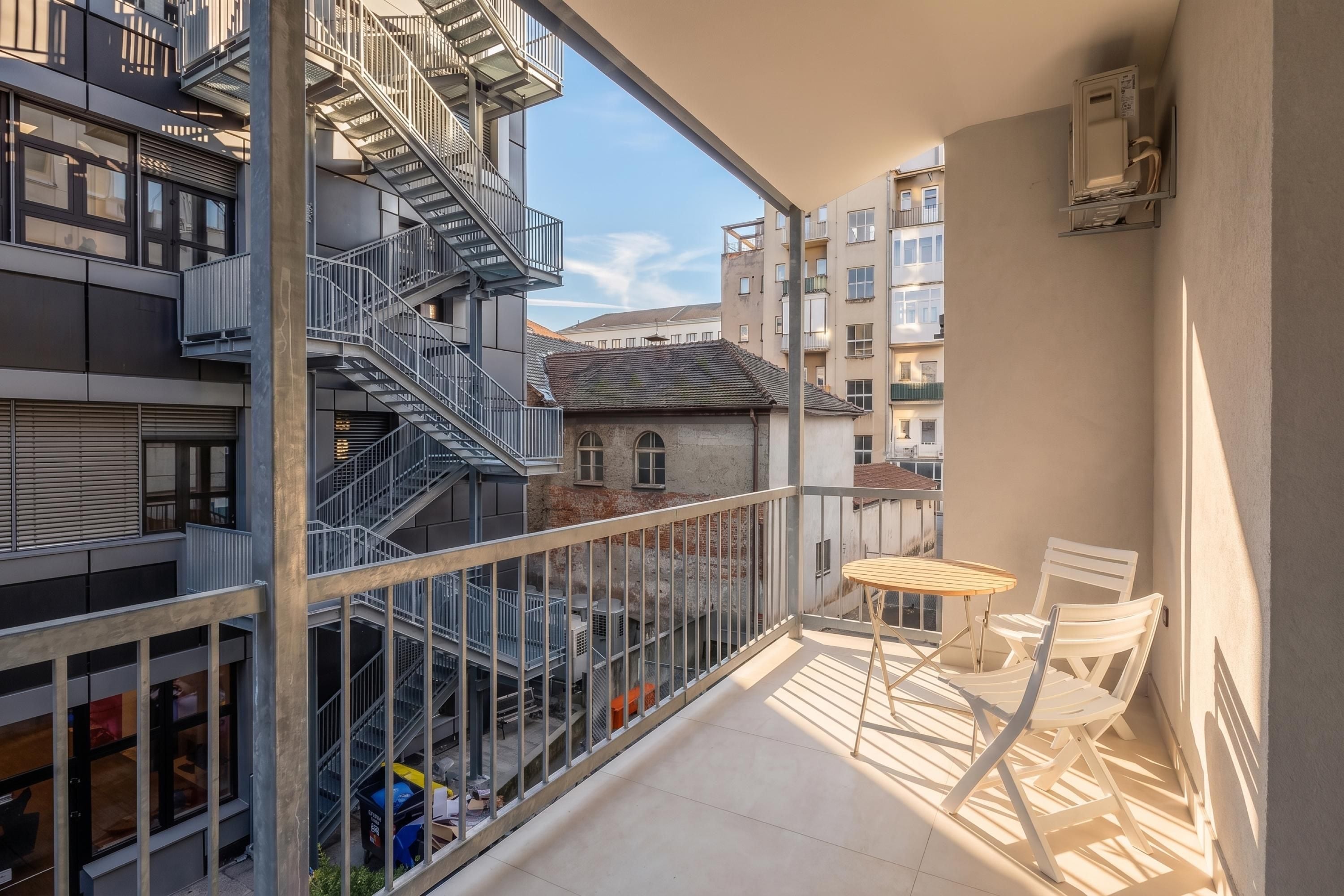 Un balcone con vista sulla città, con una scala in metallo e un tavolo con sedie.