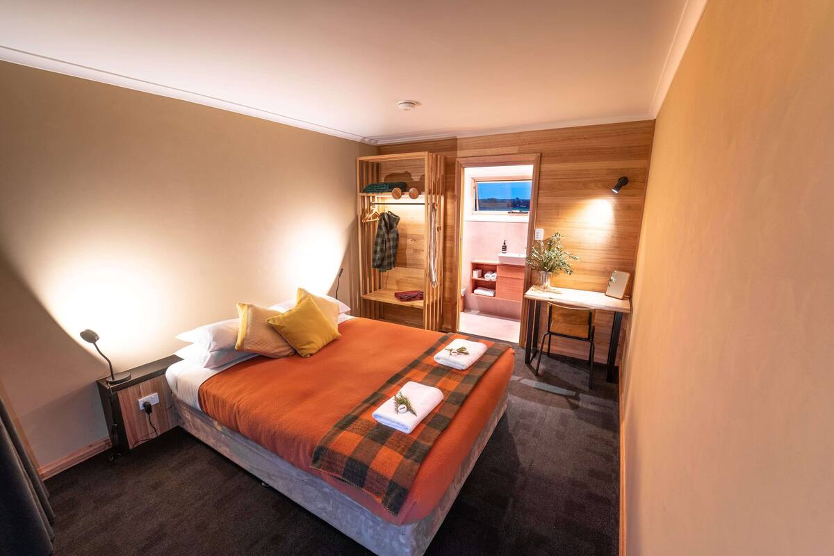 A bedroom with a bed, bedside table, and a view of the outside.