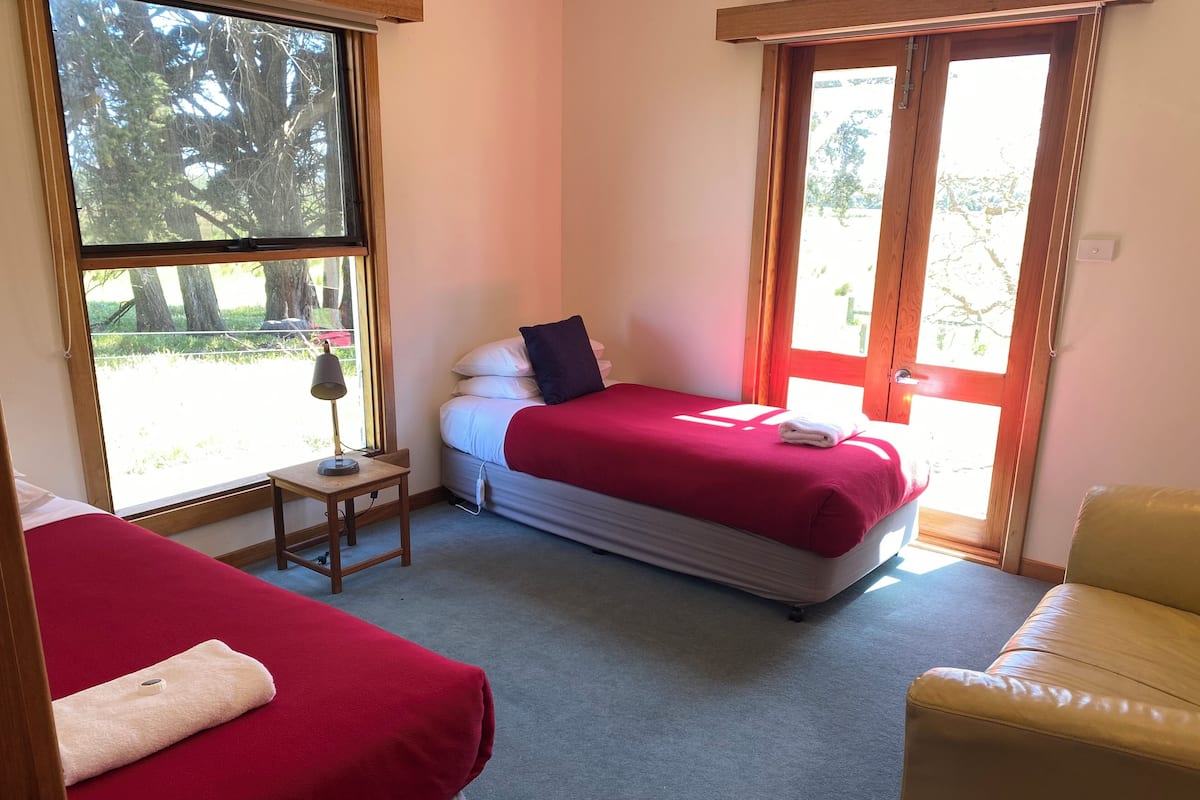 A bedroom with two beds, a small table, a chair, and a window with a view of trees.