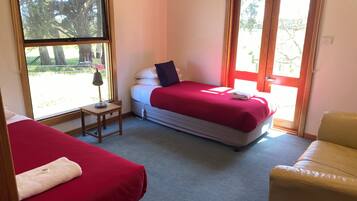 A bedroom with two beds, a small table, a chair, and a window with a view of trees.