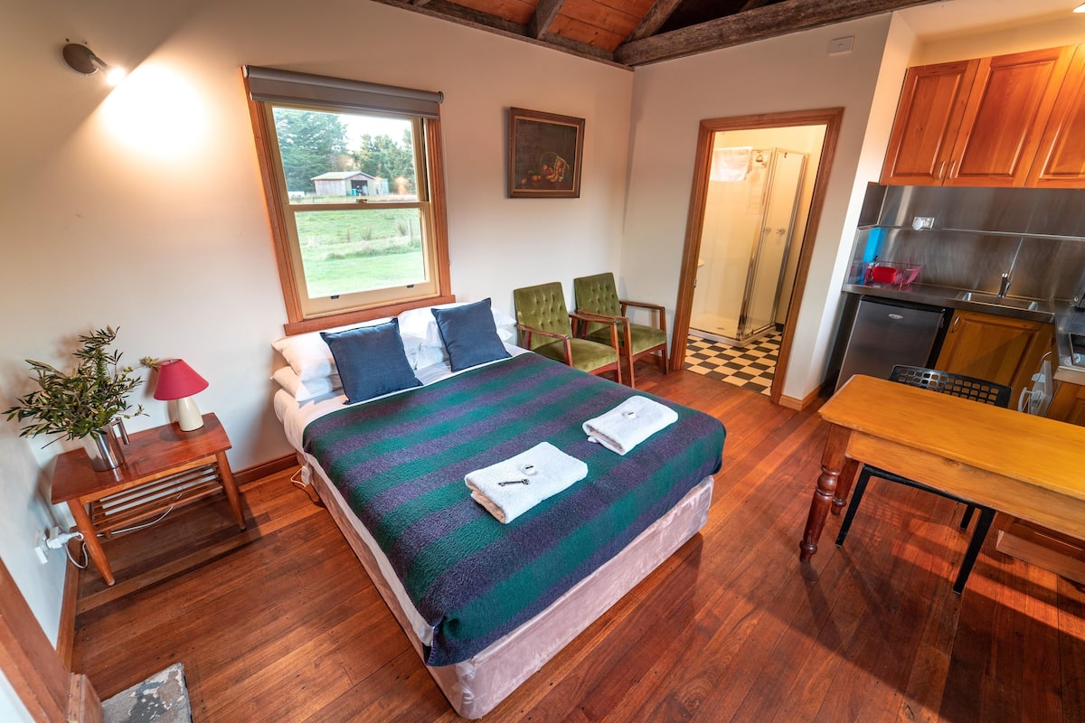 A bedroom with a bed, bedside table, lamp, and a view of the outside.