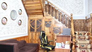 A room with a brown sofa, a black and yellow gaming chair, a wooden desk, and a staircase with patterned carpet. - BEST GUESTHOUSE (Tashkent)