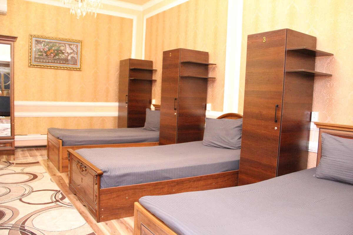 A hotel room with three wooden beds, a wooden wardrobe, and a framed picture on the wall.