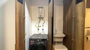 Une salle de bain compacte, composée d’une seule pièce, avec un lave-linge et un sèche-linge intégrés, un lavabo et un petit panier à linge.