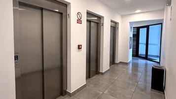Un pasillo moderno con tres ascensores, un detector de incendios y un ventanal al final.