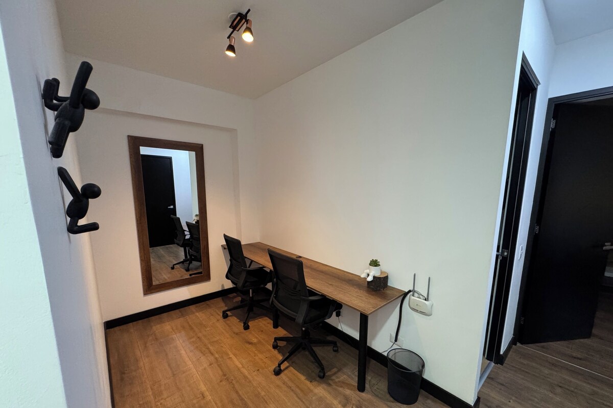 Un espace de bureau moderne avec un bureau en bois, des chaises de bureau noires, un grand miroir et une petite plante en pot.