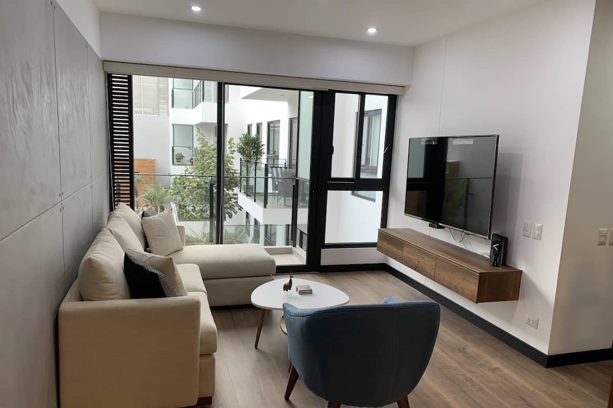 Un salon moderne avec un canapé, un fauteuil bleu, une table basse et un téléviseur.