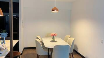 A dining area with a round table, six chairs, a vase with flowers, and a pendant light.