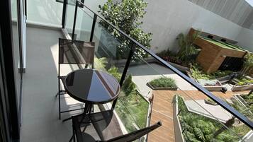 Un balcón moderno con barandilla de vidrio, una mesa de comedor con sillas y vistas a un jardín ajardinado.