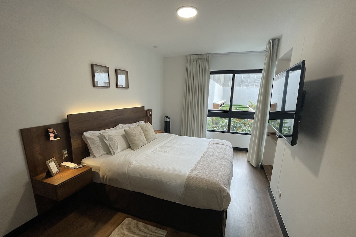 Une chambre d’hôtel avec un lit, une table de chevet, une lampe et un téléviseur fixé au mur.