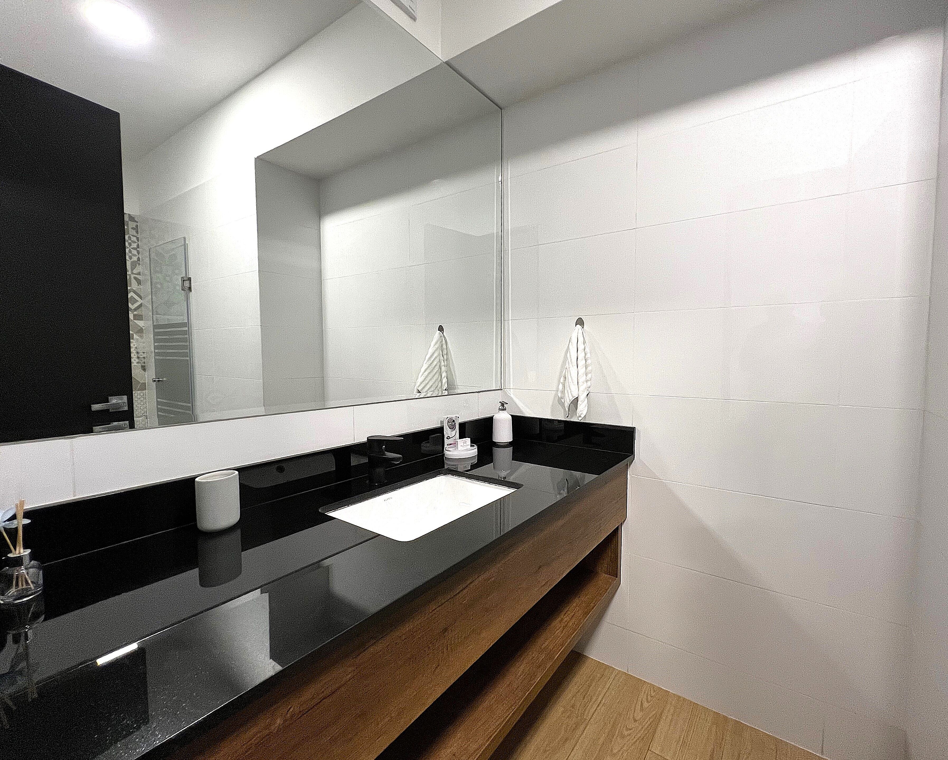A modern bathroom with a black countertop, a mirror, and white tiles.