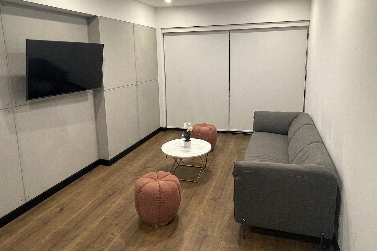 Un salon moderne avec un canapé gris, une petite table ronde et deux poufs roses.