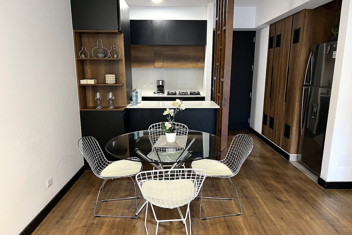 Une cuisine moderne avec une table ronde en verre et des chaises à structure métallique, des armoires en bois et un four encastré.