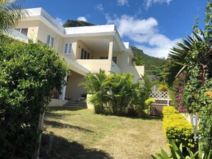 A modern two-story house with a flat roof, surrounded by lush greenery and a mountain in the background. - Black River Villa Turquoise 3bdr, sea View (Black River)
