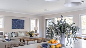 Un salon moderne avec un canapé, une table basse et un coin repas agrémenté d’un vase de fleurs et d’oranges.
