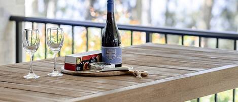 A wooden table with a bottle of wine, two glasses, a box of chocolates, and a corkscrew.
