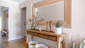 Une console en bois avec un miroir, un vase contenant des fleurs séchées, une petite plante et deux paniers blancs.