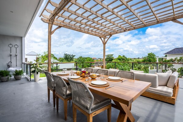 A covered outdoor dining area with a wooden table, wicker chairs, and a cushioned sofa. - Villa Ozkar - Elegant 3 Bedroom Villa with Pool & Sunset Terrace (Canggu)