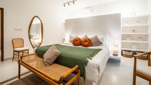 Un dormitorio moderno con una cama grande, una mesita de noche, una silla, un espejo y una estantería con objetos decorativos.