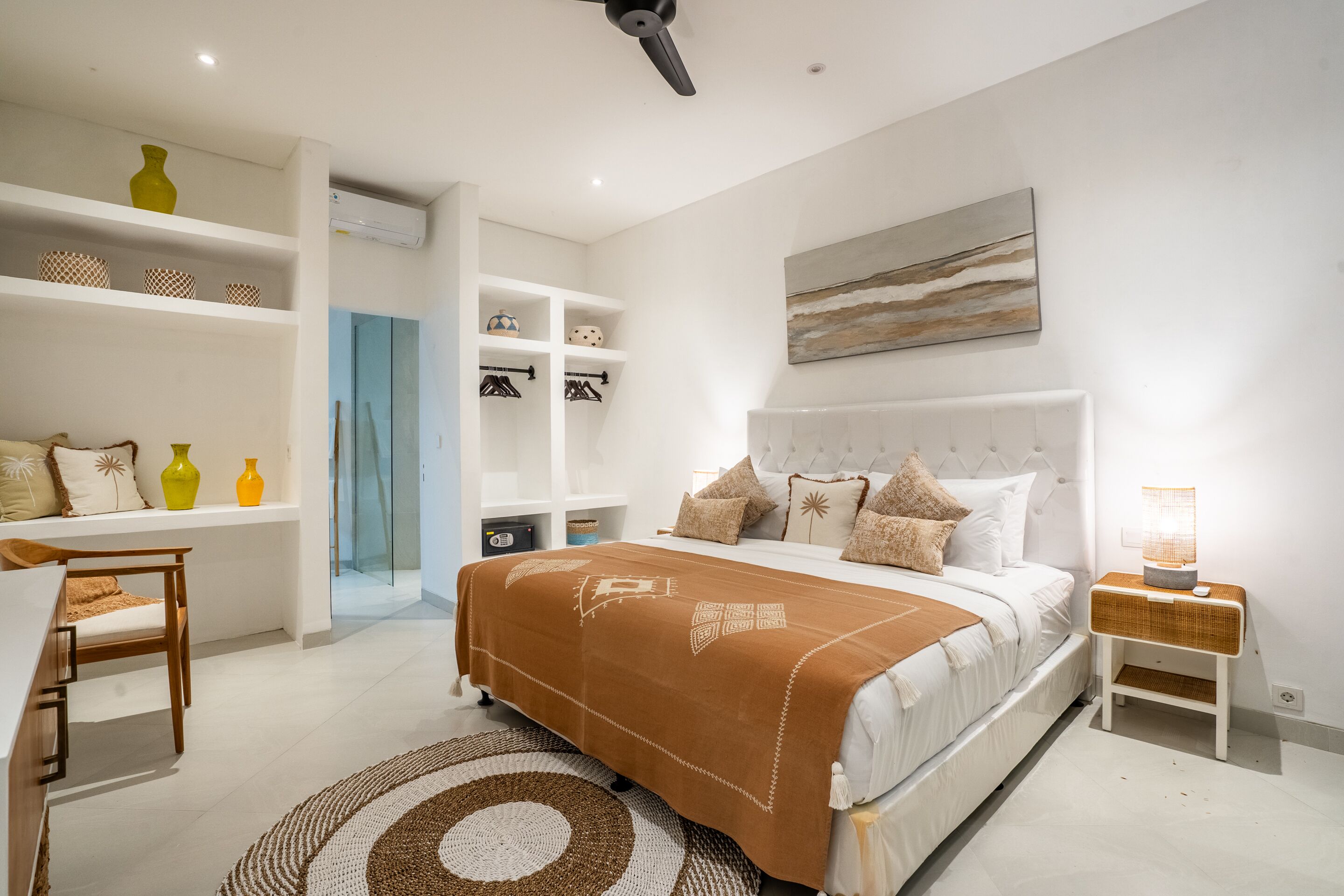 A bedroom with a bed, bedside tables, a desk, shelves, and a painting on the wall.