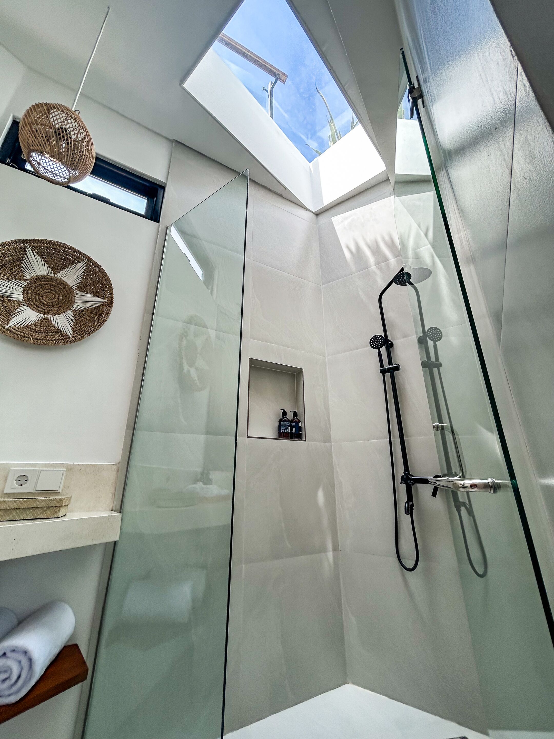 A modern bathroom with a skylight, a glass shower enclosure, and a small shelf with toiletries.