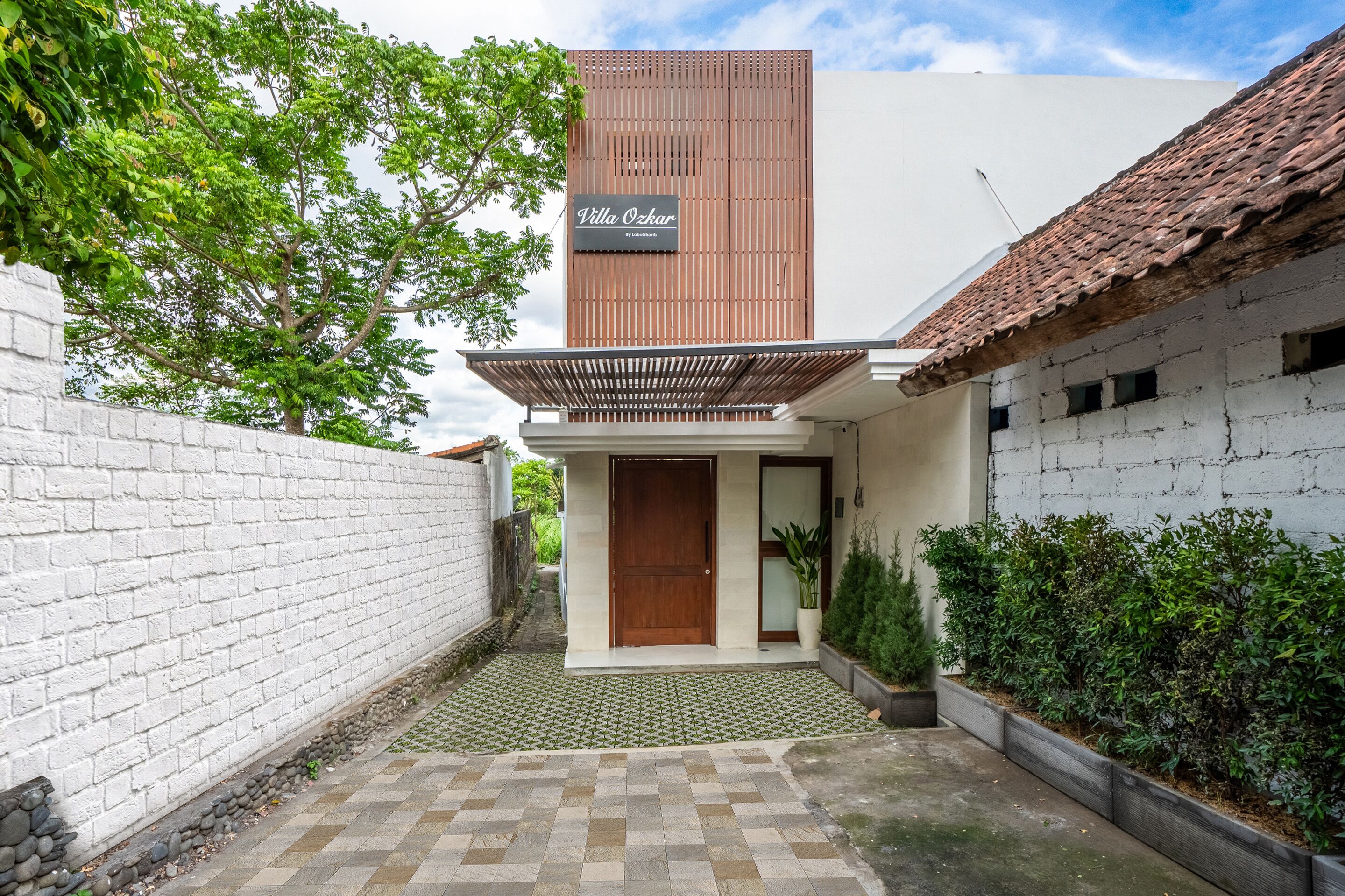 A modern villa with a wooden facade, a tiled courtyard, and a white brick wall.
