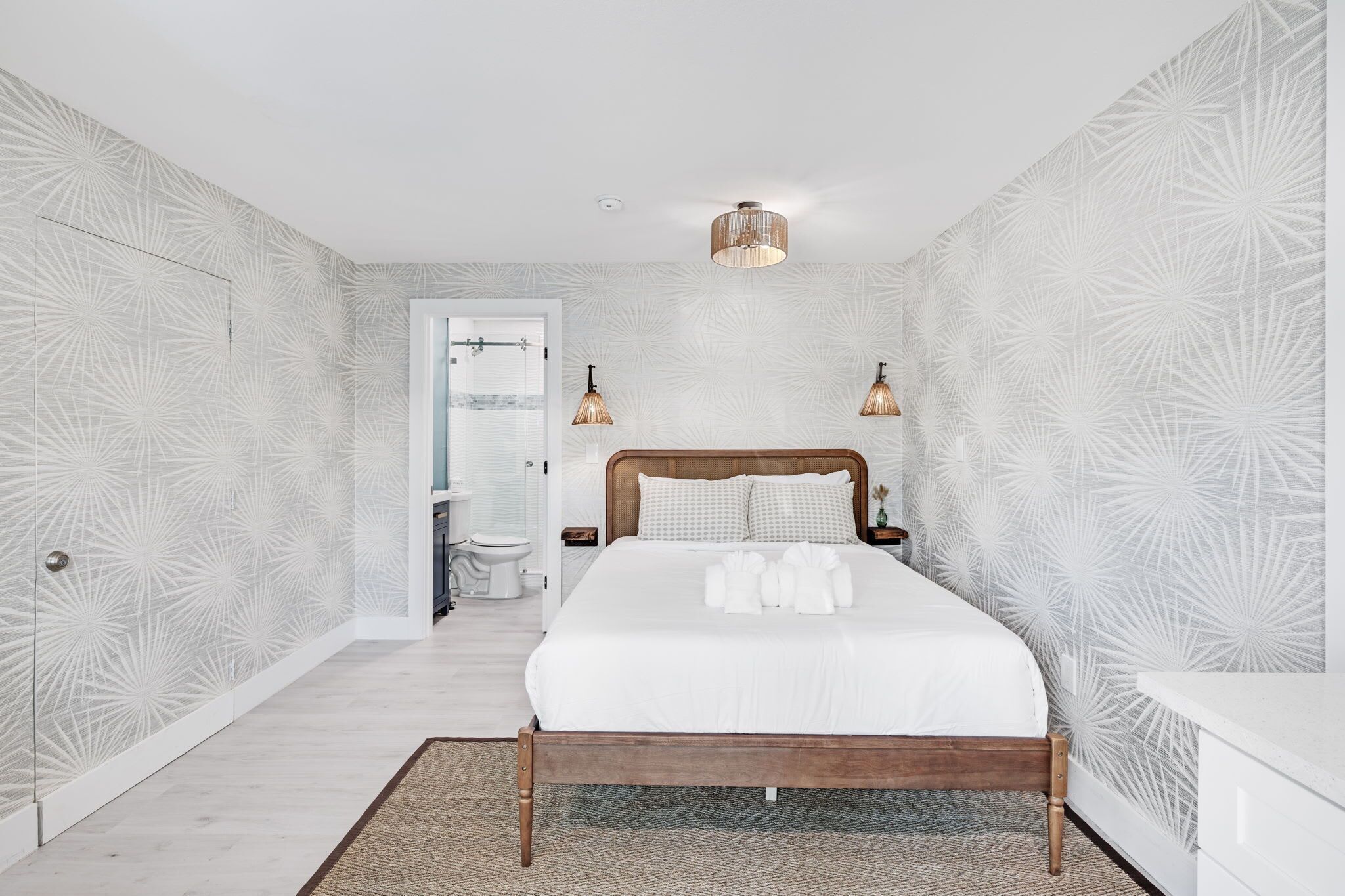 A bedroom with a bed, bedside lamps, a wooden headboard, and a patterned wall.