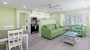Un ambiente compatto con angolo cottura, un divano verde, un tavolo da pranzo con sedie e una ventola a soffitto.