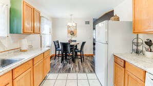 Una cocina con armarios de madera, encimera de granito, una mesa de comedor con sillas y un refrigerador.