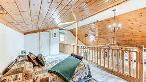 Una habitación con techo de madera, una cama con edredón estampado, una manta de color verde y una barandilla de madera con vistas a un espacio exterior.