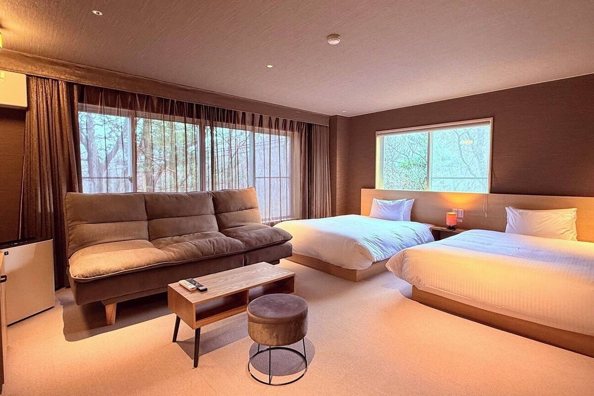 Une chambre d’hôtel moderne avec un canapé, deux lits simples, une petite table et un pouf rond.